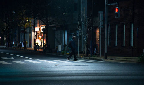 Man walking on illuminated city street at night