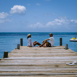 People sitting on pier looking at sea against sky