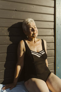 Portrait of young woman sitting on wooden wall