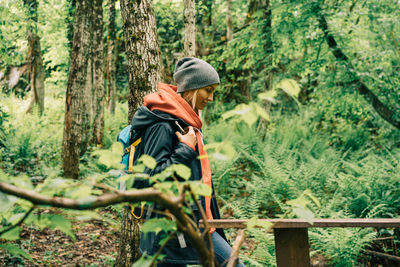 A young caucasian woman in a raincoat and a hat walks along a path in the thickets of the forest