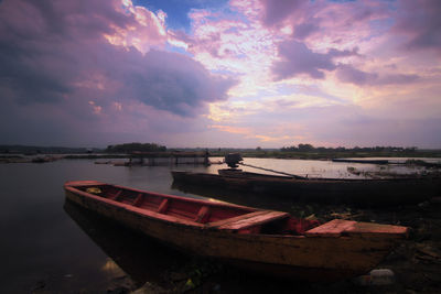 Boat moored on shore against sky during sunset