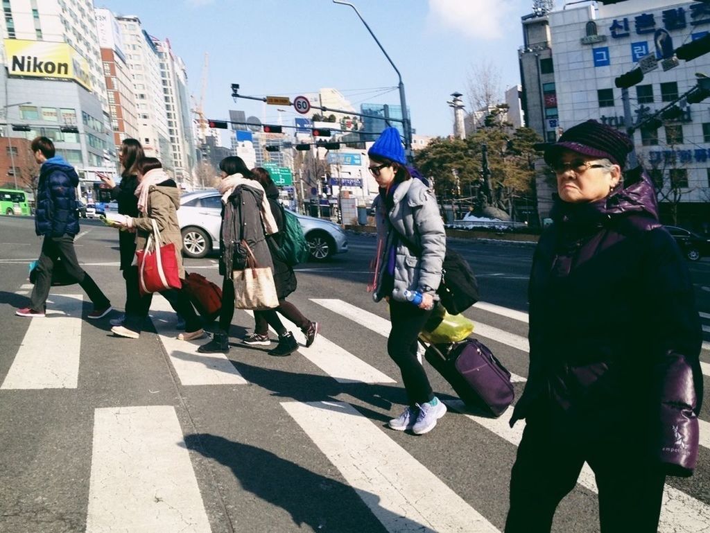 building exterior, street, city, lifestyles, architecture, built structure, city life, full length, casual clothing, men, leisure activity, walking, person, city street, road, sunlight, large group of people, togetherness, day