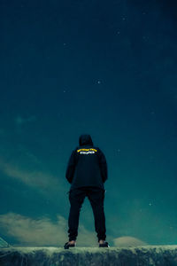 Rear view of man standing in snow against sky at night