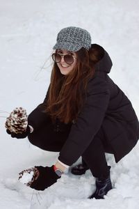 Portrait of smiling young woman crouching on snow covered land