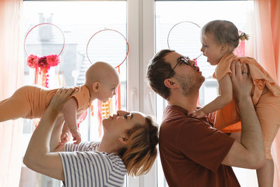 Mother and father holding children in the air over decorated with dreamcatchers sunny window at home