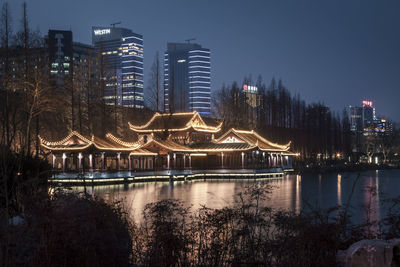 Illuminated city by river against sky at dusk