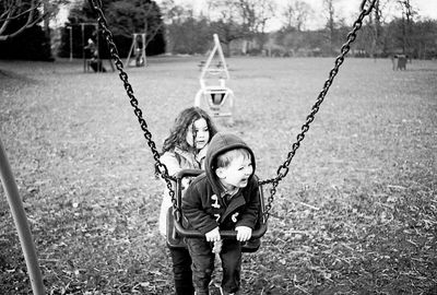 Sister pushing boy swinging at playground