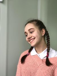 Thoughtful young woman smiling while standing against wall