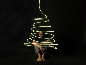 Man sitting amidst spiral illuminated light against black background