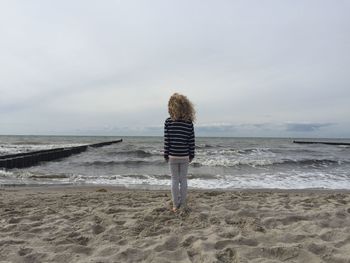 Rear view of woman standing on beach against sky