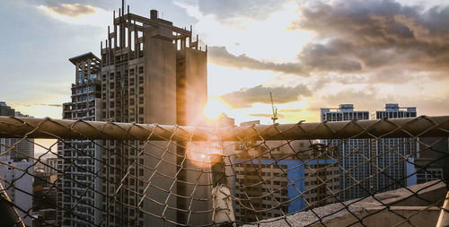 Sunlight streaming through chainlink fence against sky during sunset