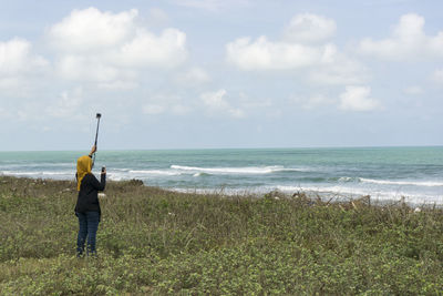 Rear view of man standing on beach against sky