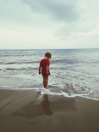 Boy standing on beach against sky