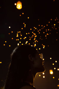 Low angle view of woman standing against illuminated lanterns at night