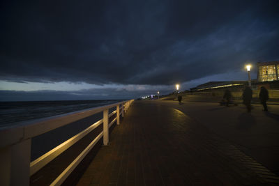 Illuminated footpath by sea against sky at night