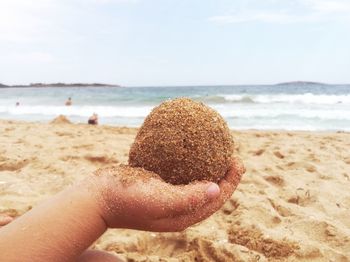 Close-up of hand holding sand at beach against sky