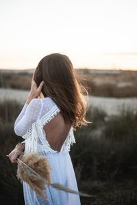 Rear view of woman standing on field against sky during sunset