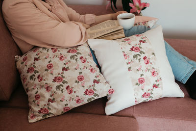 Low section of woman reading book sitting on sofa at home