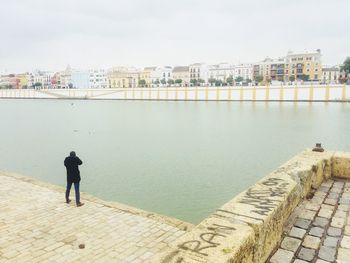 Man standing by river in city against sky