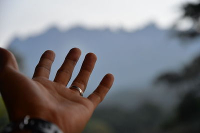 Close-up of hand gesturing against sky
