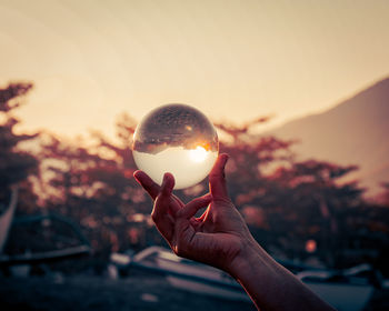 Person holding crystal ball against sky during sunset