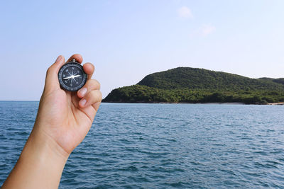 Cropped hand holding navigational compass against sky