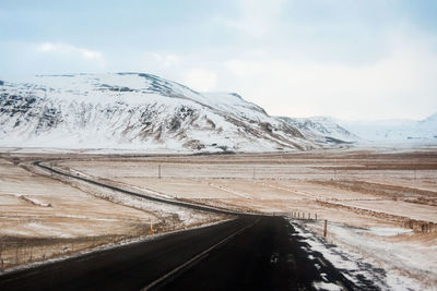 Empty road amidst landscape leading towards snowcapped mountain against sky