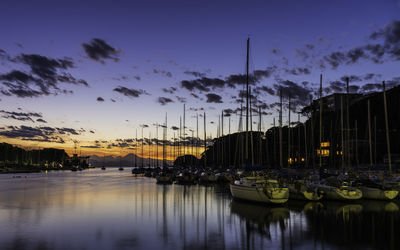 Sailboats moored at harbor against sky during sunset