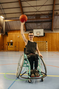 Smiling girl balancing basketball while sitting on wheelchair at sports court