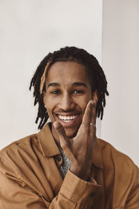 Portrait of smiling man touching cheek against white background