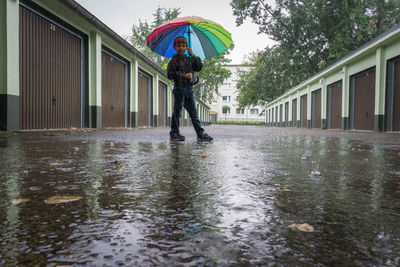 Boy holding multi colored umbrella on road amidst closed stores during rain