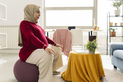 Pregnant woman learning online yoga on laptop in living room