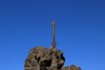 Low angle view of cross on rock against blue sky