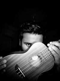 Portrait of young woman playing guitar against black background