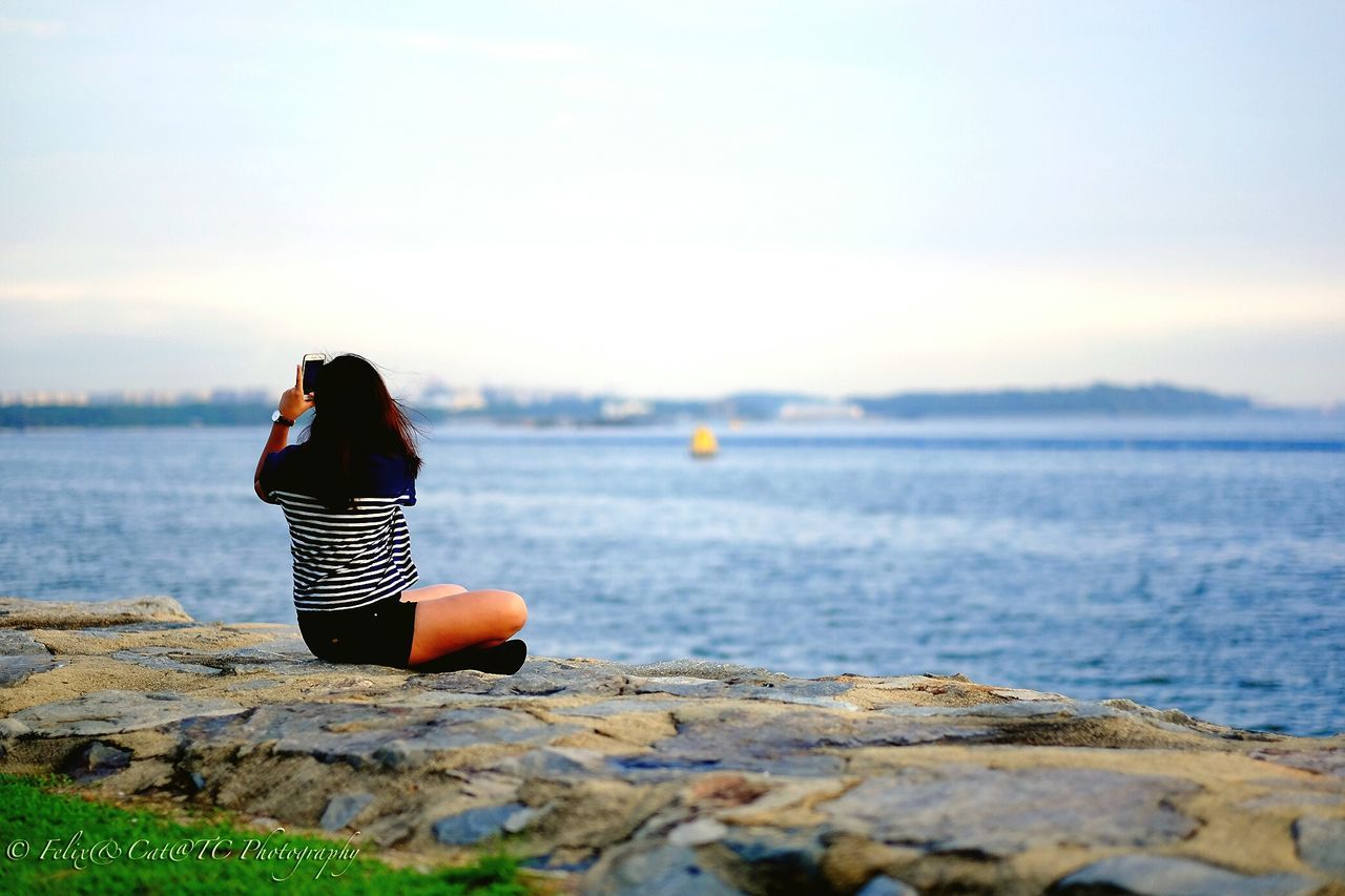 REAR VIEW OF WOMAN SITTING ON SHORE