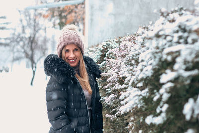 Portrait of smiling young woman standing against snow during winter