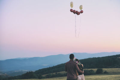 Rear view of young couple standing on field against sky during sunset