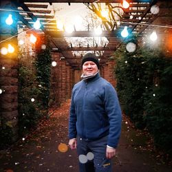 Portrait of young man standing against illuminated lights at night