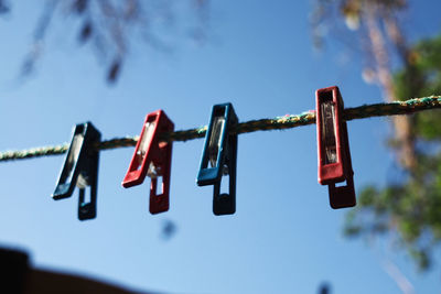 Low angle view of clothespins hanging on clothesline against blue sky