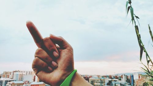 Close-up of hand against sky in city