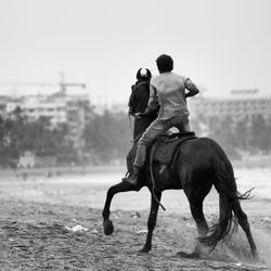Rear view of a man riding horse on beach