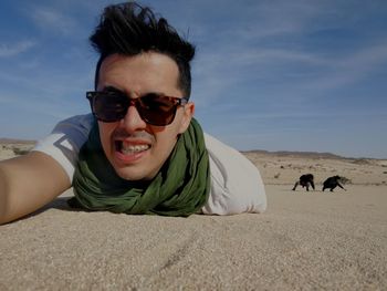 Portrait of man wearing sunglasses lying on desert