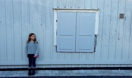 Full length of girl looking away while standing against house