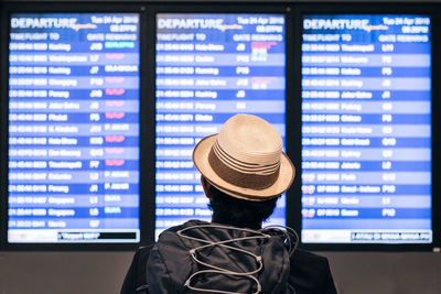 Rear view of man wearing hat looking at device screens at airport