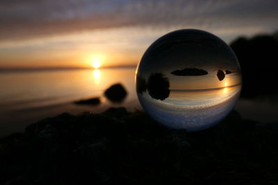 Close-up of crystal ball on beach against sky during sunset