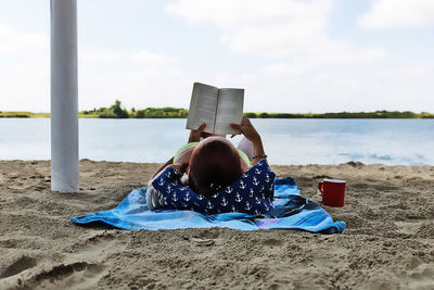 Man sitting on beach by sea against sky