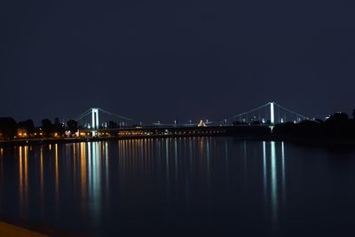 Illuminated bridge over river against sky at night