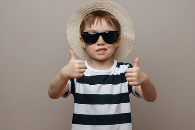Portrait of boy wearing sunglasses standing against gray background