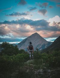 Rear view of young man standing on mountain against sky during sunset