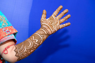 Cropped hand of bride with henna tattoo against blue background